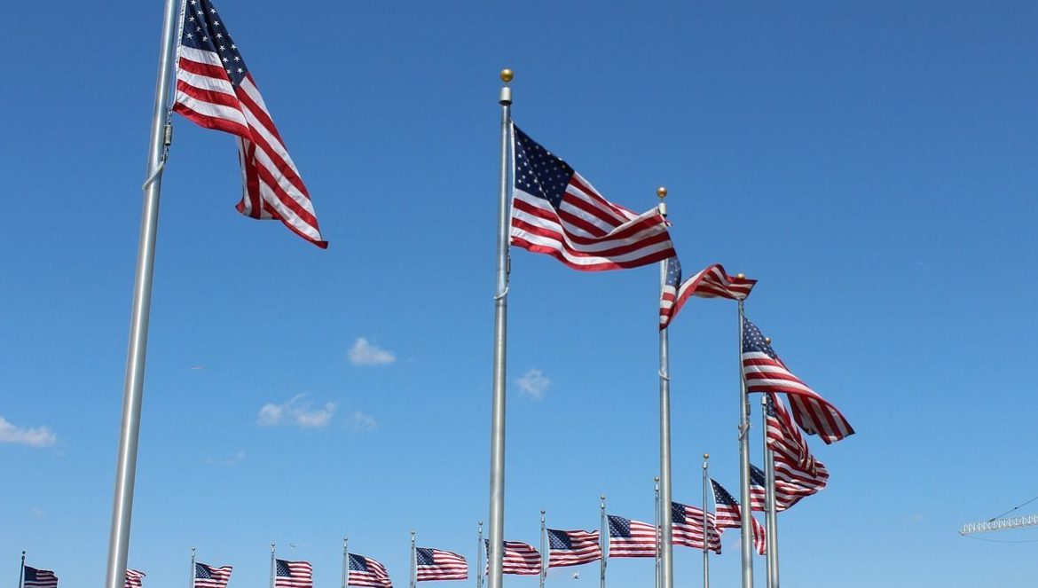 U.S. flags waving in the wind against the backdrop of a blue sky.